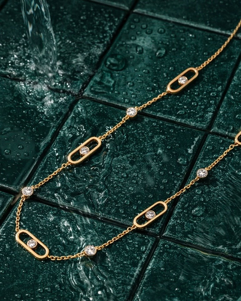 The Glimmer Chain a thin gold chain with diamond like accents on a velvet deep jade green flat lay