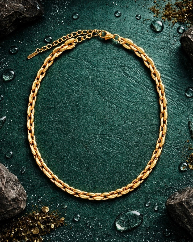 The bean chain a coffee bean style gold chain on a flat deep jade green background with earthy elements