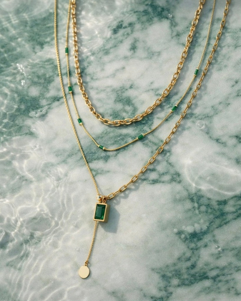 The intrigue stack a 3 chain necklace stack on a green and white marble background with water droplets