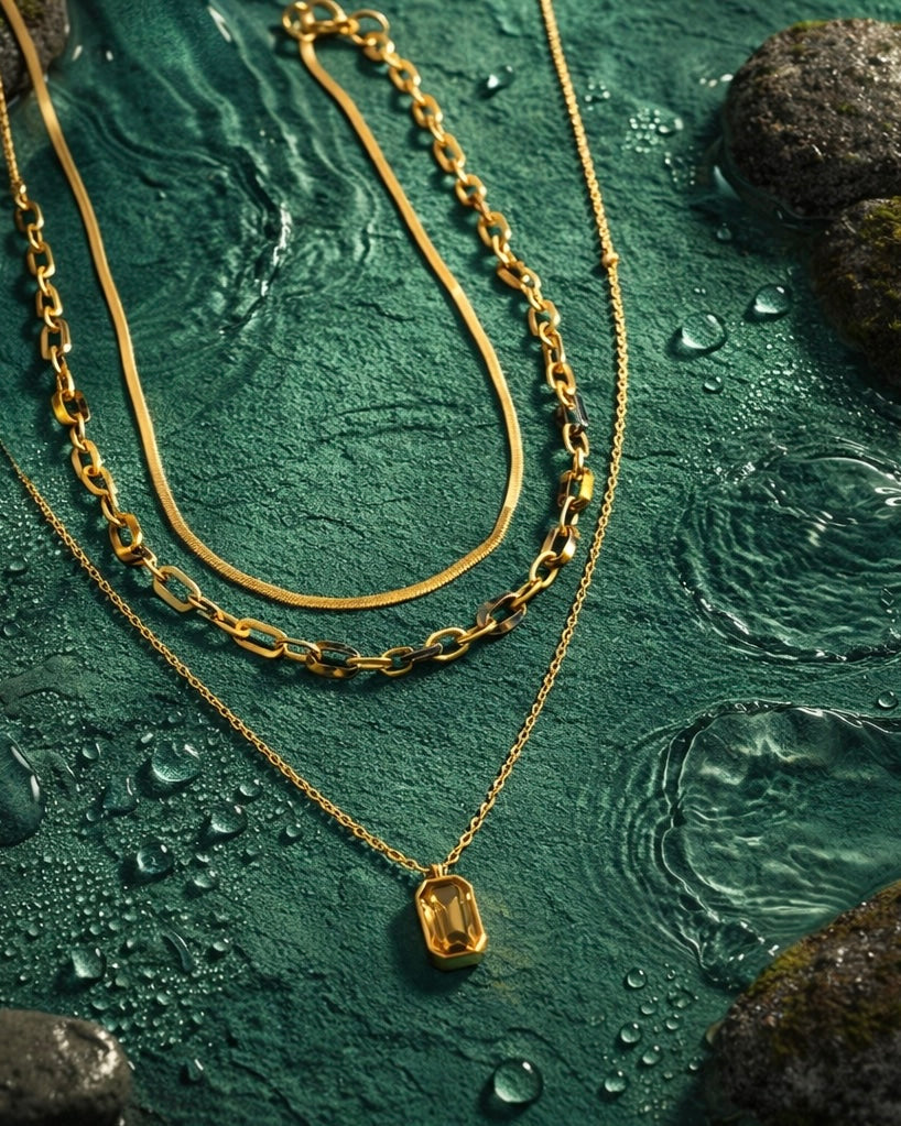 The aura stack a collection of 3 necklaces on a jade green earthy background with water droplets